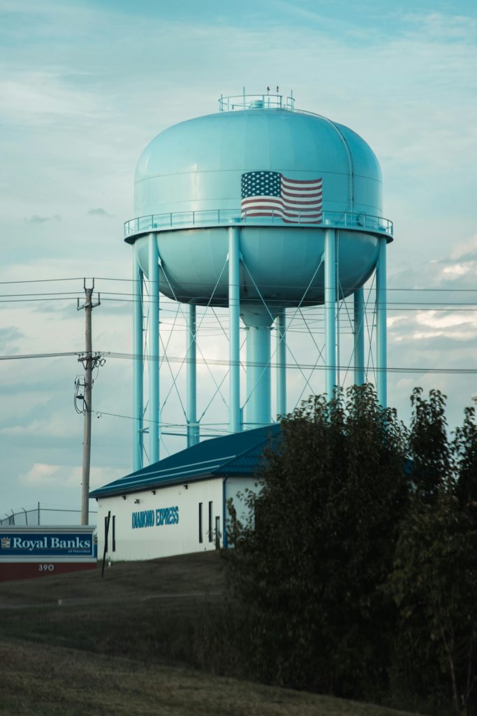 A large blue water tower with an American flag in a rural landscape.